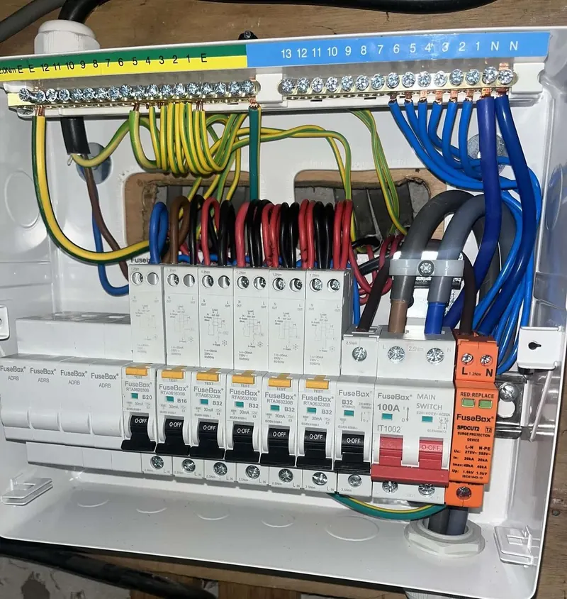An open FuseBox consumer unit fitted by DL Electrical Services, with a row of RCBOs, a red 100A main switch and an orange surge protection device