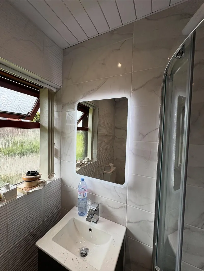 Backlit LED mirror above the sink in a marble-tiled bathroom