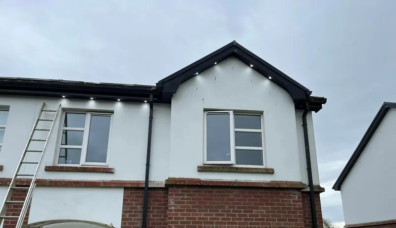 A white rendered house with new LED downlights set into the soffits along the eaves and around the gable
